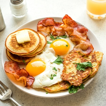 Amerikansk morgenmad med sunny-side æg, hash browns, bacon og pandekager